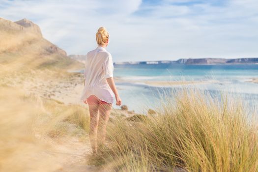 Relaxed woman in white shirt looking at distance, enjoying beautiful nature, freedom and life at serene landscape at Balos beach, Greece. Concept of vacations, freedom, happiness, joy and well being.