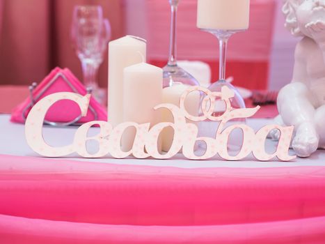 Word wedding in Russian language, white letters on dinner table in pink colors. Wedding decor. Caption wedding of letters. Celebrating wedding ceremony