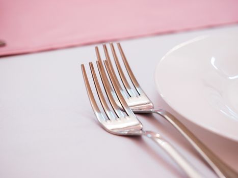 Two kitchen forks on dinner table with pink tablecloth