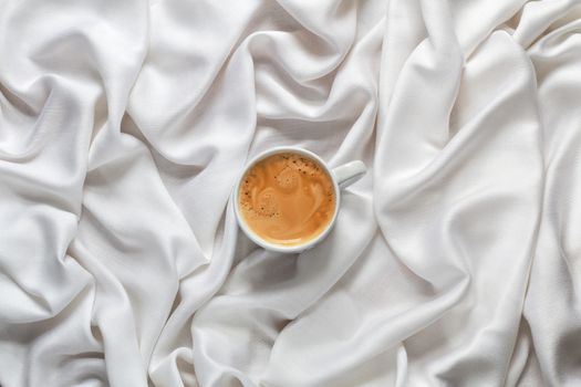 Cup of coffee on a white silk fabric. Espresso with froth in the form of smiley face and scattered beans. Top view.