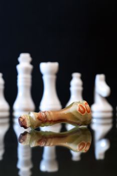 Chess Queen made from Onyx lying before lot of chessmen against dark background