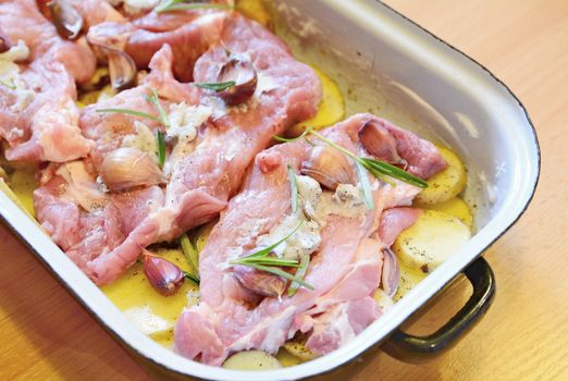 Raw pork neck chops with potatoes slices, rosemary and garlic in pan. The meal is prepared for baking.