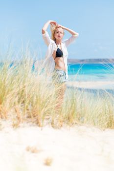 Relaxed woman wearing unpinned white shirt and black bikin, enjoying sun, freedom and life an a beautiful beach. Young lady feeling free, relaxed and happy. Concept of health well being.