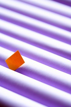 Individuality concept. One yellow small paper square between set of violet paper tubes