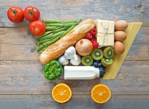 Fruits, vegetables, pasta and dairy products in the shape of a grocery cart icon over a wooden backdrop