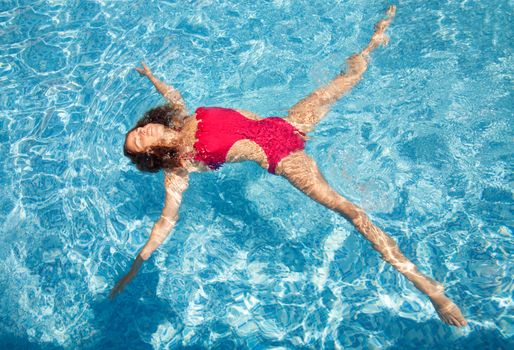Beautiful young woman laying back on water in pool, star position - relaxed under the sun.