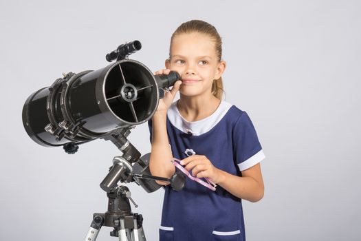 Seven-year girl standing next to a reflector telescope and looks mysteriously into the sky