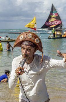 Pernambuco, Brazil July 6, 2016: An unidentified singer in Chicken Beach with typical sail boats behind in Ipojuca City near barrier reef, northeast Brazil