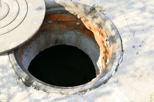 Concrete cesspit with an open hatch on the ground in the summer.