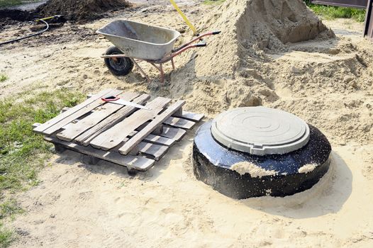 Construction site with new armed manholes, cart, sand and equipment.