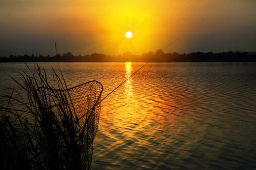 Fishing rod and tank against the sunset on the lake at night fishing