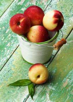 Heap of Perfect Ripe Small Nectarines in White Garden Bucket closeup on Green Wooden background
