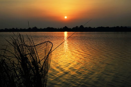 Fishing rod and tank against the sunset on the lake at night fishing
