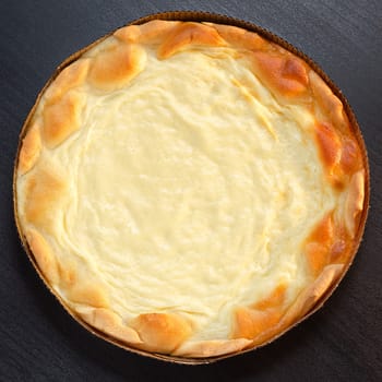 Pie with sour cream on a black wooden surface, in a cardboard baking pan