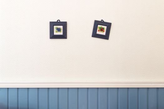 Two small square pictures of blueberries and strawberries in frames hanging on the white and blue wall