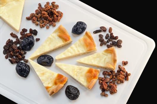 Slices of sour cream cake and dried fruit lying on a white cutting Board, isolated on black background