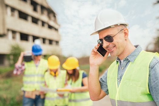 Construction architects using phone in front building damaged in the disaster.