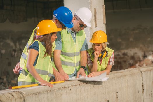 Four construction architects review plan in front building damaged in the disaster.