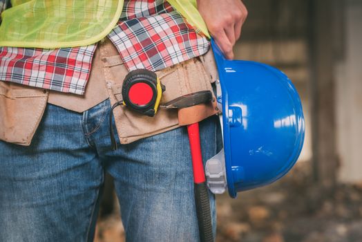Close-up of a construction worker with blue helmet and tool belt at construction site.