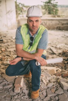 Construction architect holding plans and looking at camera in building damaged in the disaster.