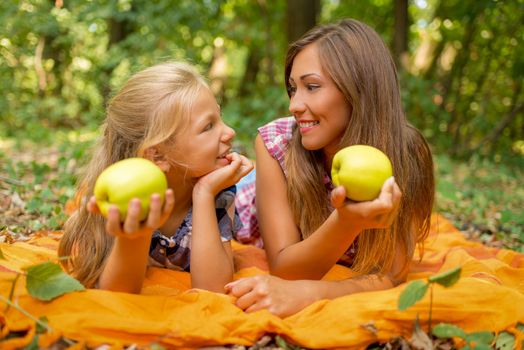 Beautiful young mom and her little girl lying in a forest and enjoying. 