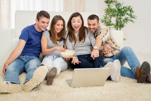 Four cheerful best friends having nice time in an apartment. They are watching movie together.