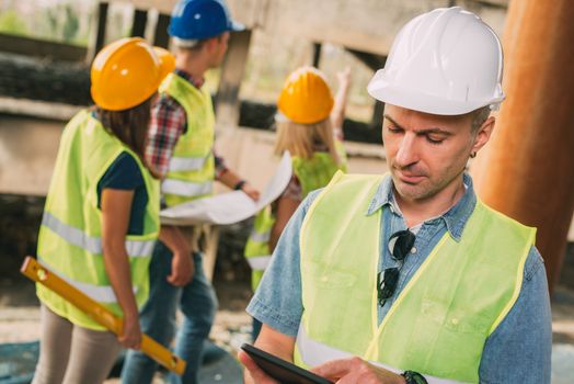 Construction architects using digital tablet in building damaged in the disaster. His colleagues review plan.