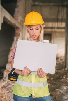 Beautiful young female construction architects holding a blank white board in building damaged in the disaster. 