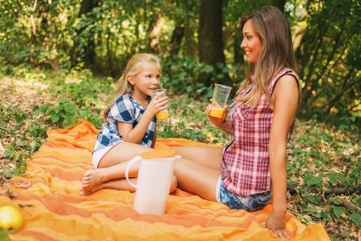 Beautiful young mom and her little girl sitting in a forest and enjoying. 