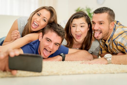 Four cheerful best friends having nice time in an apartment and taking selfie.