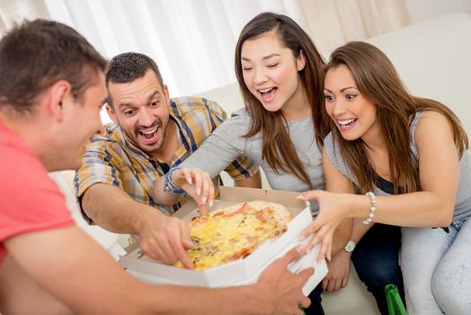 Four cheerful friends enjoying pizza together at home. Selective focus.