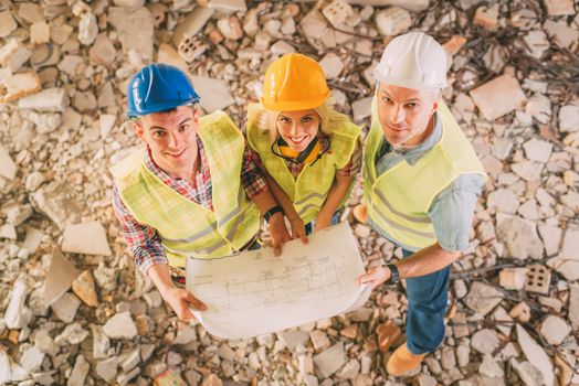 Three construction architects review plan in building damaged in the disaster. Looking at camera.