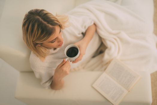 Beautiful young woman relaxing with cup of coffee and reading a book.