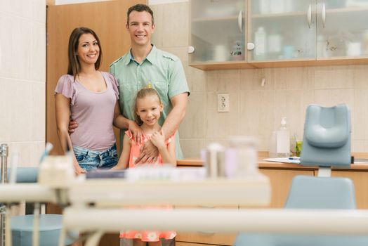 Happy young family at visit in the dentist office. They are standing and looking at camera.