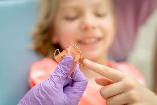 Close-up of a dentist showing mobile orthodontic appliance the little girl patients. Selective focus. Focus on foreground, on mobile orthodontic appliance for dental correction.