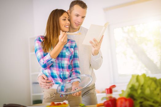 Beautiful young couple cooking healthy meal in the domestic kitchen. They reading recipe in the cookbook.