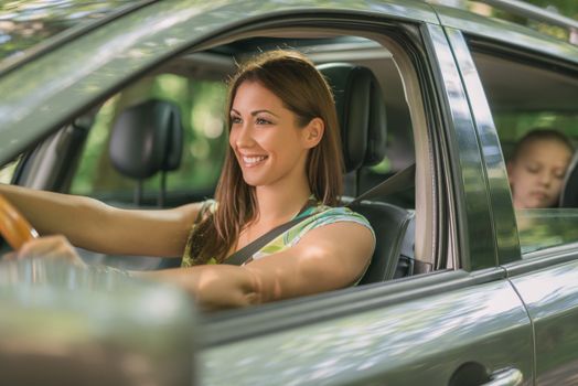 Young beautiful woman with a nice smile driving a car.  Her cute daughter sitting on rear and enjoying.