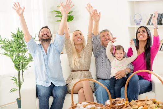 Happy family sitting on couch with arms raised and looking up. In front of them are baskets with pastries.