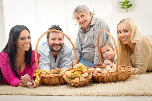 Happy family lying on a carpet in the living room around woven baskets filled with baked goods and looking at camera.