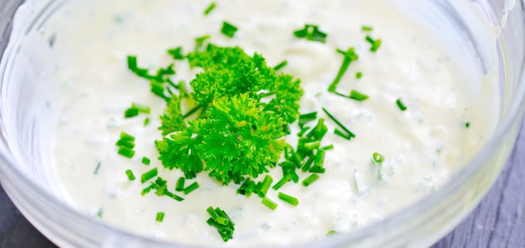 Glass bowl with garlic sour cream dressing sprinkled with fresh parsley.