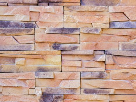 a wall from an artificial beige and gray stone facade with rough fractured surfaces