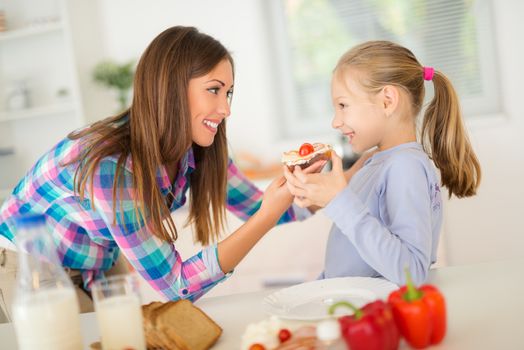 Beautiful mother and her daughter having breakfast in the domestic kitchen.