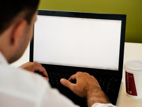 Man using laptop with blank screen on desk in cafe interior.