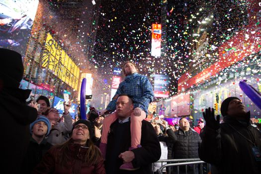 UNITED STATES, New York: A child sitting on a man's shoulders smiles through the confettis of celebrating new years after ringing in the new year in Times Square on January 1, 2016 in New York City. The New York Police Department will have more than 6,000 officers in the Times Square area, including more than 1,100 officers who graduated from the police academy on Tuesday. It will be the largest such deployment of police in New York City ever. 
