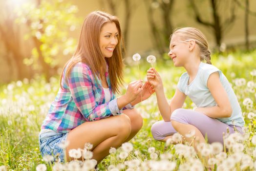 Happy cute little girl with mother holding dandelions in the park.