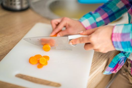 Close-up of a female hands cutting carrot on the kitchen board.