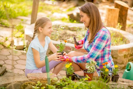 Cute happy little girl assisting her mother planting flowers in a backyard.