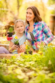 Cute little girl assisting her mother planting flowers in a backyard. Looking at camera.