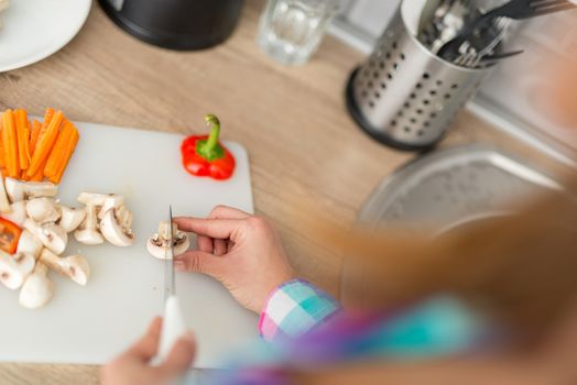 Close-up of a woman hands cutting vegetarian food on the kitchen board. Rear view.