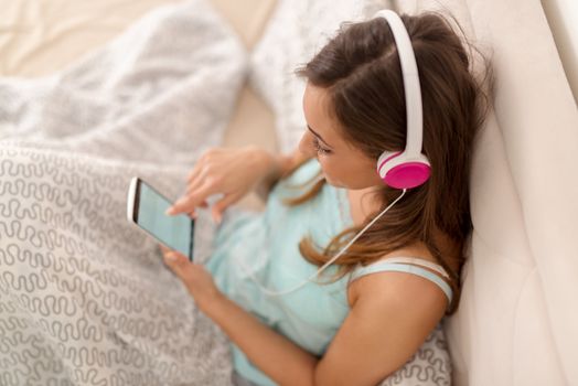 Beautiful smiling girl relaxing in bed and listening music. Selective focus.